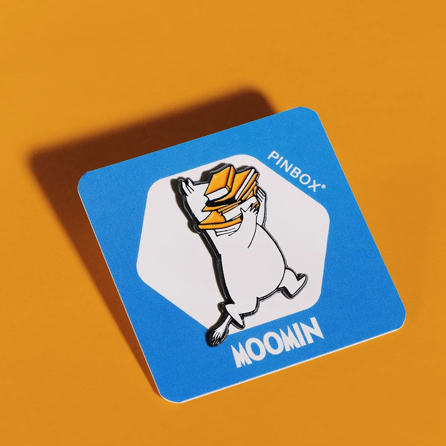 Emaliowany pin przedstawiający muminka w minimalistycznym czarno-białym designie, biegnącego ze stosem pomarańczowych książek